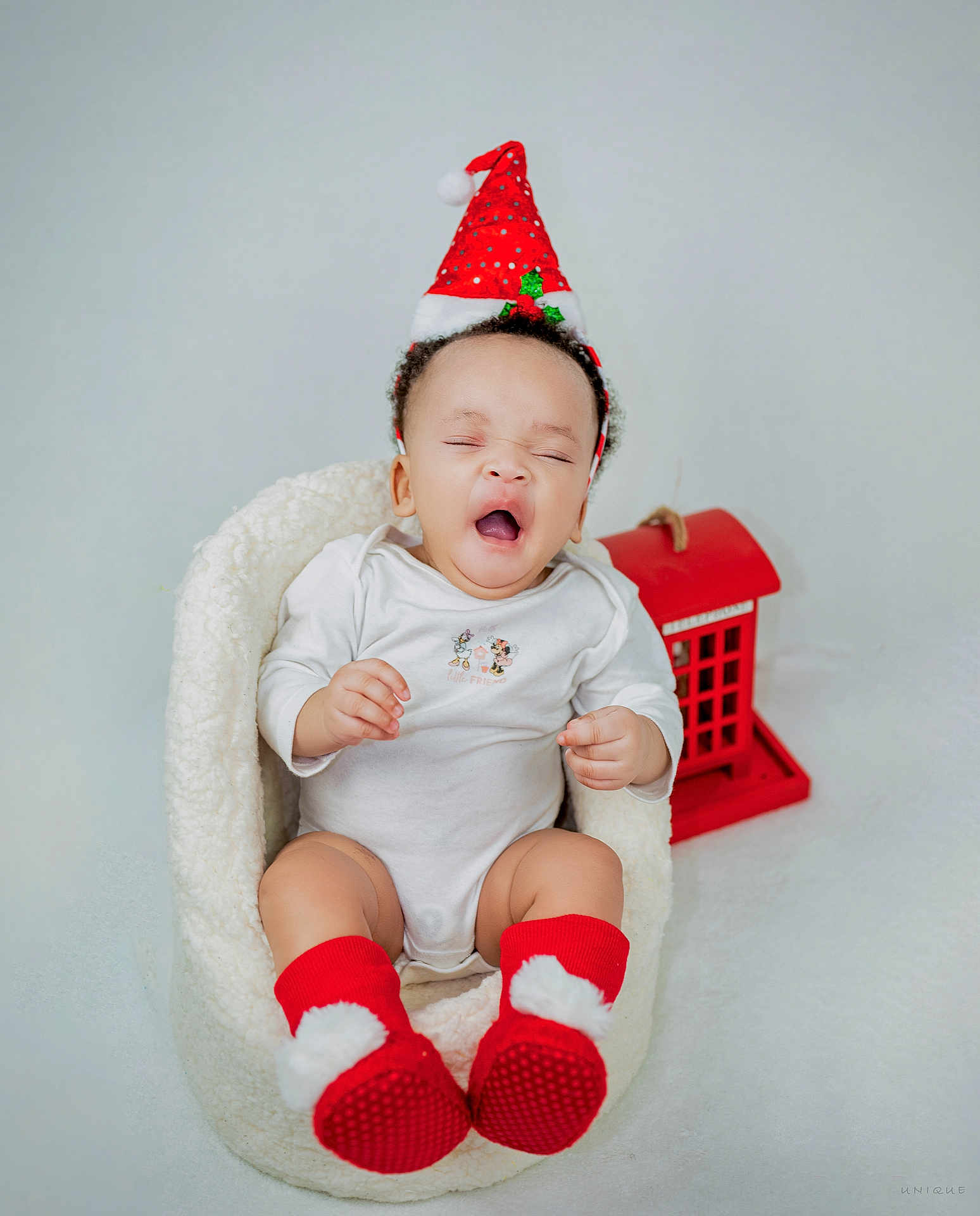 Eliora is registered to the contest to win money with this photo: baby, infant, santa_hat, red_socks, yawning, white_onesie, cozy_seat, decorative_house, holiday_theme, cute, indoor, child, portrait, festive, smiling, soft_texture, holiday_decor, adorable, sitting, young_child