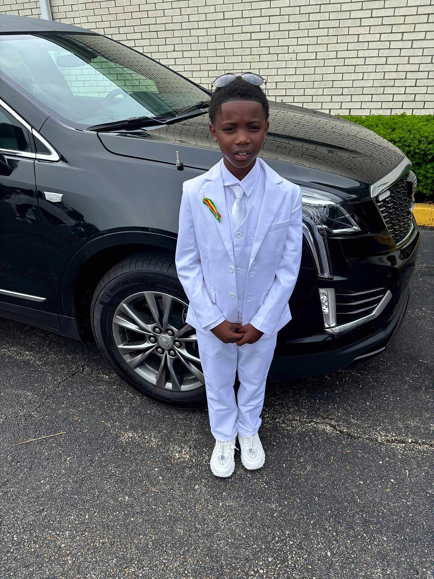 Antwon joined the competition — help win amazing prizes! child, boy, white_suit, tie, sunglasses, car, black_suv, pavement, parking_lot, ribbon, formal_wear, shoes, urban, outdoor, portrait, standing, person, vehicle, tire, headwear