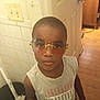 Antwon is registered to the contest to win money with this photo: child, boy, sunglasses, indoor, tiled_wall, door, wooden_floor, tank_top, casual_clothing, person, portrait, expression, standing, looking_up, eyewear, light_switch, bucket, floor, room, home