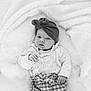 baby, infant, headwrap, knitted_sweater, checkered_pants, blanket, soft_texture, cozy, cute, portrait, newborn, child, hands, face, lying_down, monochrome, black_and_white, warmth, expression, indoors