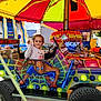 amusement_park, canopy, car, child, colorful, entertainment, event, fun, happy, inflatable_slide, mural, outdoor, person, play, ride, smiling, spiderman, tent, toy, vehicle