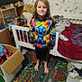 barefoot, bed, bedroom, bird_pattern, blanket, bookshelf, butterfly_pattern, cardboard_box, carpet, child, colorful_rug, hoodie, indoor, long_hair, person, smiling, stitch, stuffed_animal, toy, wallpaper