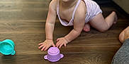 Audri is registered to the contest to win money with this photo: baby, crawling, floor, wooden_floor, toys, purple_toy, blue_toy, couch, living_room, person, child, curious, indoors, skin, clothing, infant, cute, expression, head, hands