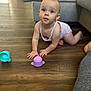 baby, crawling, floor, wooden_floor, toys, purple_toy, blue_toy, couch, living_room, person, child, curious, indoors, skin, clothing, infant, cute, expression, head, hands