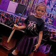 Alianna is registered to the contest to win money with this photo: child, birthday, party, face_paint, toy_sword, costume, skirt, boots, smiling, standing, indoor, decorations, streamers, gift_bags, poster, music_theme, purple, black_clothing, wood_floor, portrait