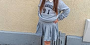 Kathaleya participe au concours pour gagner de l'argent avec cette photo : child, girl, standing, gray_sweatshirt, gray_skirt, black_sneakers, hair_bows, sidewalk, concrete_wall, urban, casual_clothing, portrait, young_person, outdoor, street, hands_on_hips, confident, serious_expression, fashion, daylight