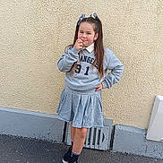 Kathaleya participe au concours pour gagner de l'argent avec cette photo : child, girl, pigtails, grey_sweatshirt, grey_skirt, black_sneakers, socks, posing, outdoor, wall, asphalt, urban, casual_clothing, standing, confident, young, fashion, portrait, daylight, playful