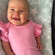 Mila is registered to the contest to win money with this photo: baby, smiling, infant, pink_clothing, blanket, stars_pattern, happy, face, lying_down, cute, child, soft_texture, portrait, skin, hand, head, cheeks, person, toddler, indoors
