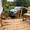 dog, porch, wooden_floor, pickup_truck, grass, trees, chair, collar, outdoor, house, backyard, vehicle, nature, daylight, relaxed, canine, leash, fence, rural, quiet