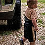 toddler, child, side_view, shorts, crocs, gravel, outdoor, vehicle, truck, tire, walking, curly_hair, casual_clothing, daytime, nature, grass, small_person, young_child, exploring, profile