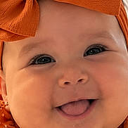 Angel joined the competition — help win amazing prizes! baby, child, infant, portrait, smiling, happy, tongue_out, orange, bow, headband, dress, patterned_clothing, jewelry, earring, close_up, face, eyes, indoor, photography, cute