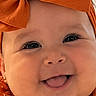 baby, child, infant, portrait, smiling, happy, tongue_out, orange, bow, headband, dress, patterned_clothing, jewelry, earring, close_up, face, eyes, indoor, photography, cute