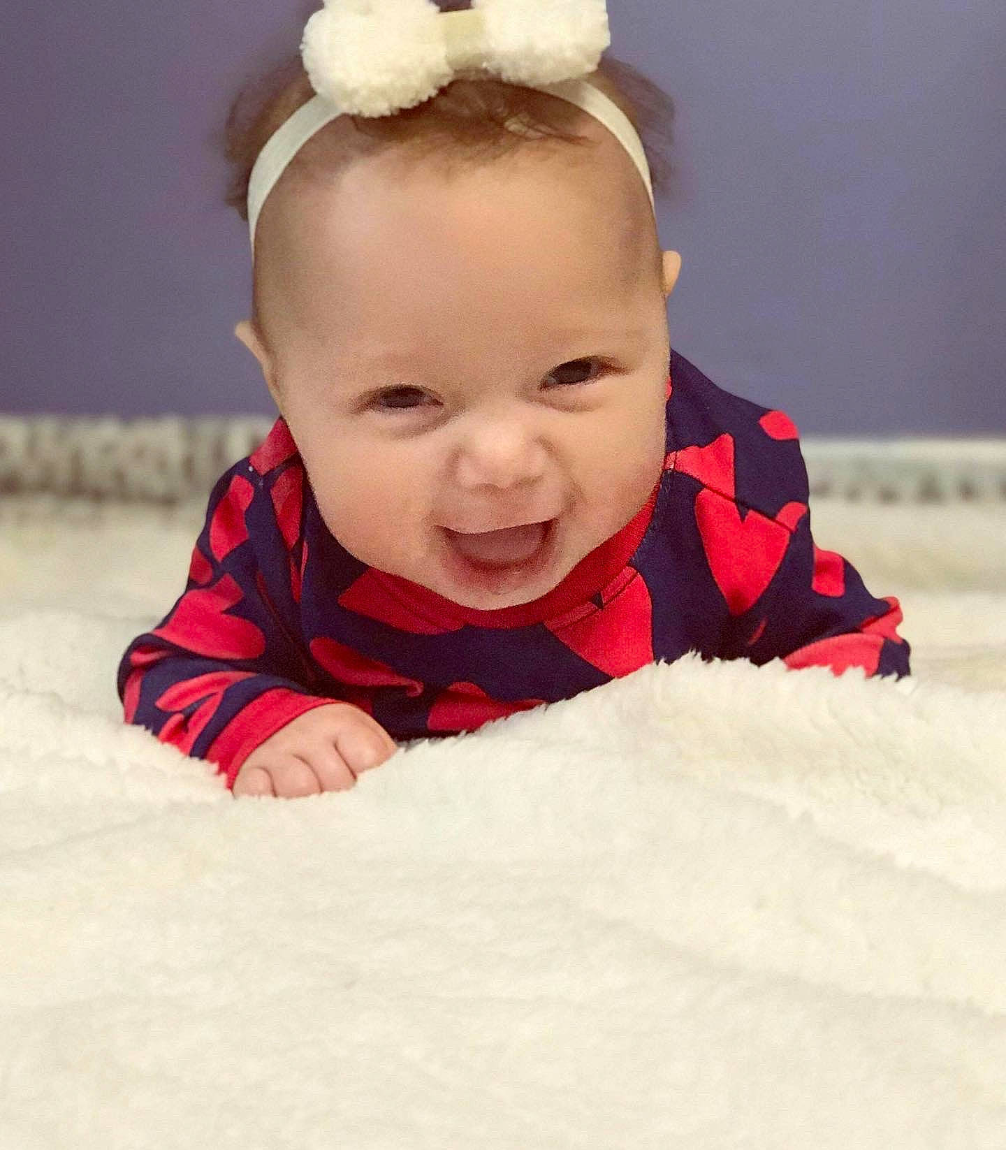 Aila is registered to the contest to win money with this photo: baby, beauty, cheek, child, crawling, ear, eye, face, facial_expression, forehead, hair_accessory, head, lip, nose, person, pink, skin, smile, toddler, tummy_time