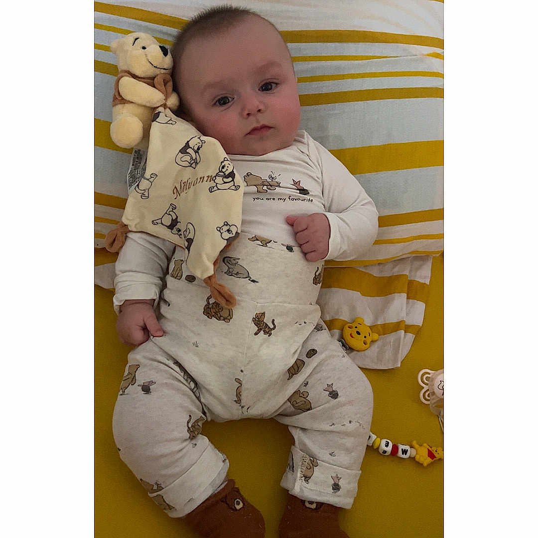 Mëlyann participe au concours pour gagner de l'argent avec cette photo : baby, bed, child, cozy, cute, face, footwear, hand, indoors, infant, lying_down, pajamas, plush_toy, sleepwear, smiling, soft_toys, striped_pillow, white, winnie_the_pooh, yellow