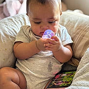 Aiden is registered to the contest to win money with this photo: baby, infant, child, pacifier, sitting, couch, cushion, blanket, smartphone, portrait, indoor, home, curious, focused, hands, gray_clothing, bare_legs, soft_lighting, photography, cozy