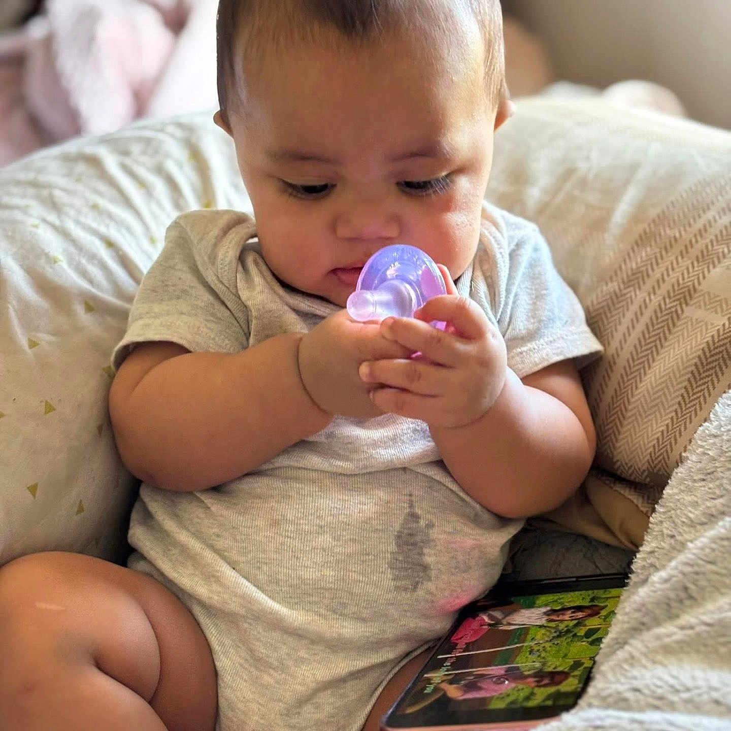 Aiden is registered to the contest to win money with this photo: baby, infant, child, pacifier, sitting, couch, cushion, blanket, smartphone, portrait, indoor, home, curious, focused, hands, gray_clothing, bare_legs, soft_lighting, photography, cozy