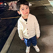 Arin is registered to the contest to win money with this photo: blue_pants, boy, car, casual_clothing, child, curious_expression, dark_hair, looking_up, night, outdoor, parking_lot, sidewalk, snow, standing, street_lights, sweater, urban, wet_pavement, white_sneakers, young_child