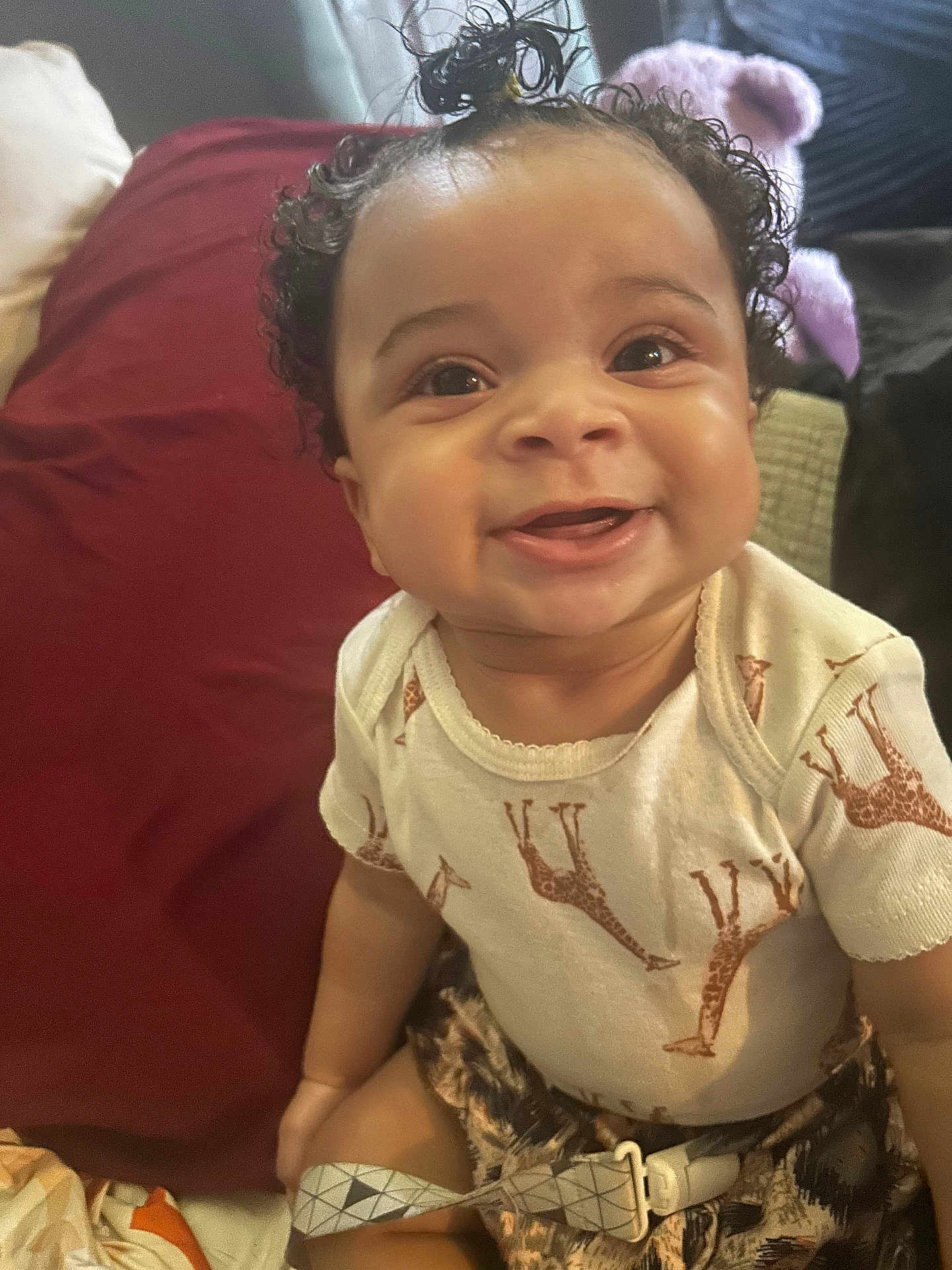 Zaierra joined the competition — help win amazing prizes! baby, child, smile, curly_hair, onesie, giraffe_print, indoor, couch, pillow, happy, portrait, infant, cute, person, seated, clothing, strap, fabric, face, young