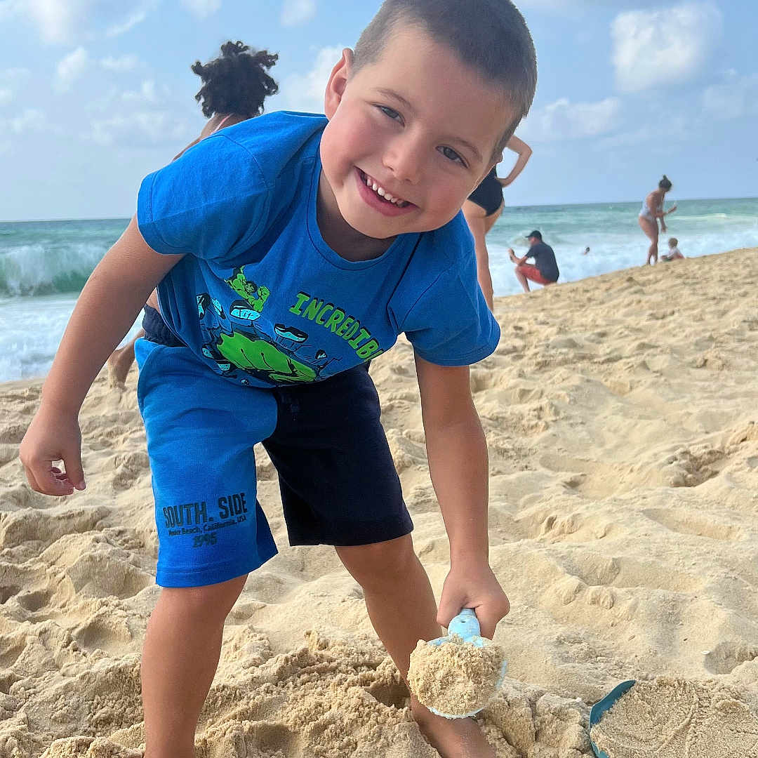 Leo participe au concours pour gagner de l'argent avec cette photo : barefoot, beach, blue_sky, boy, child, clouds, fun, ocean, outdoor, people, playing, sand, shorts, shovel, smiling, summer, sunny, tshirt, vacation, waves