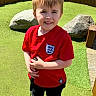 black_pants, boy, casual_clothing, child, daylight, green_grass, happy, leisure, mini_golf, nature, outdoor, playing, putter, recreation, red_shirt, rocks, shoes, short_hair, smiling, sunny
