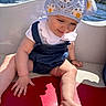 baby, child, hat, crocheted_hat, flower_pattern, smile, water, boat, outdoor, sunlight, mountain, nature, clothing, denim, white_shirt, skin, hand, foot, seat, happy