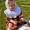 baby, child, pony, saddle, outdoor, grass, greenery, sunny, headwear, bonnet, vintage_clothing, white_socks, cute, smiling, holding, animal, pet, nature, portrait, daylight