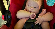 Karsten is registered to the contest to win money with this photo: baby, infant, child, car_seat, safety_harness, red, seated, sleepy, face, hands, feet, toes, toy, hanging_toy, indoors, portrait, close_up, colorful, baby_carrier, family
