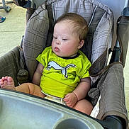 Karsten is registered to the contest to win money with this photo: baby, child, stroller, seat, green_shirt, footwear, picnic_table, outdoor, infant, person, face, head, clothing, foot, expression, curious, summer, daylight, fabric, comfort