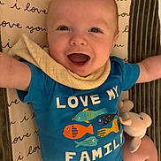 Oliver joined the competition — help win amazing prizes! baby, infant, smiling, blue_onesie, fish_graphic, text_on_clothing, blanket, plush_toy, happy, arms_outstretched, close_up, face, cute, child, indoor, laying_down, soft_toy, patterned_blanket, expression, portrait