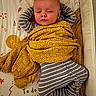 baby, sleeping, blanket, striped_clothing, crib, infant, patterned_blanket, peaceful, face, child, bedtime, resting, cute, indoor, toddler, pajamas, head, arms_up, colorful_background, soft_lighting