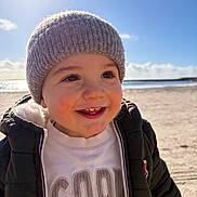 Lisandre a rejoint le concours — aidez-le/la à gagner de superbes lots ! beach, child, cozy, cute, daylight, face, happy, hat, jacket, knit_hat, outdoor, person, portrait, sand, sky, smile, sunlight, toddler, warm_clothing, water