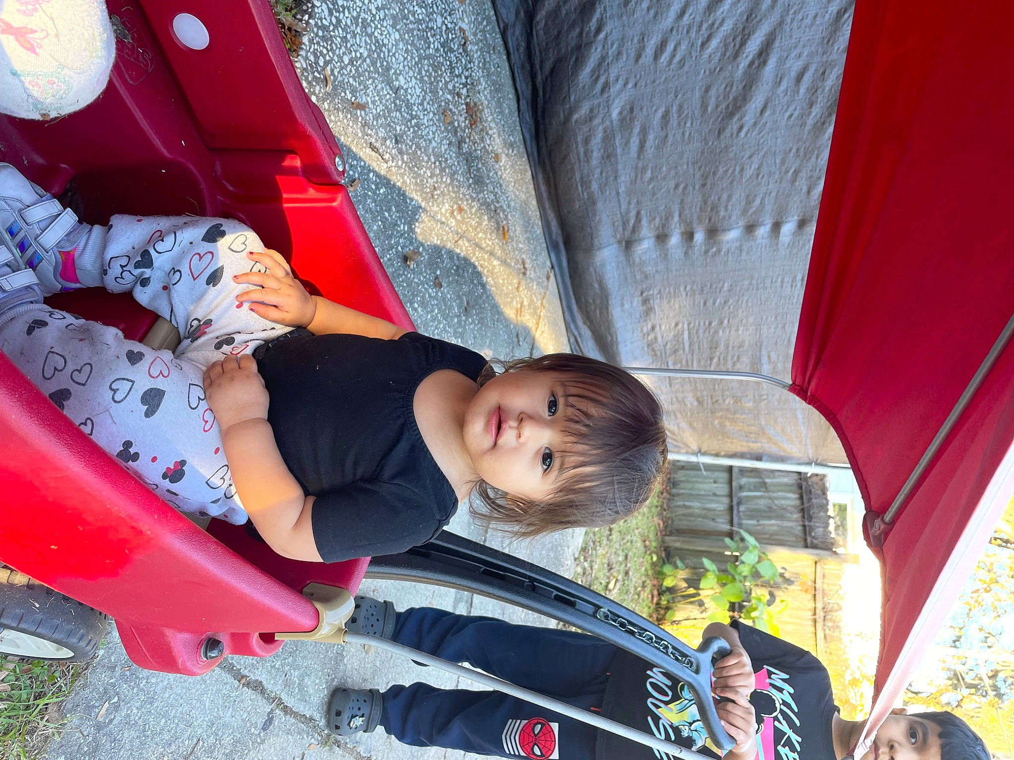 Alaïa is registered to the contest to win money with this photo: auto_part, automotive_exterior, automotive_tire, child, city, fun, grass, human_leg, leisure, motor_vehicle, person, play, recreation, sitting, smile, t_shirt, toddler, tree, vehicle, vehicle_door