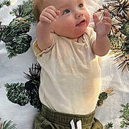 Tanner is registered to the contest to win money with this photo: baby, child, infant, portrait, lying_down, face, smiling, wide_eyed, hands, fists, cream_shirt, green_pants, clothing, blanket, pine_pattern, indoor, close_up, adorable, playful, photography