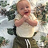 baby, child, infant, smiling, happy, portrait, lying_down, face, hands, short_sleeves, shirt, pants, clothing, blanket, pinecone_pattern, indoor, close_up, adorable, photography, joy