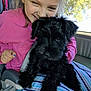 child, puppy, dog, black_dog, smiling, pink_hoodie, car_interior, seatbelt, striped_blanket, happy, curly_fur, closeup, window, sunlight, cute, pet, friendship, young_girl, indoor, cozy