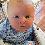 Axel joined the competition — help win amazing prizes! baby, child, infant, striped_clothing, blue_clothing, wooden_floor, indoor, curious, wide_eyes, person, face, young_child, batman_shirt, standing, flooring, furniture, table, chair, casual, candid