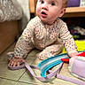 baby, child, crawling, floor, toy, onesie, indoor, wooden_floor, curious, wide_eyes, hand, face, expression, patterned_clothing, playtime, infant, closeup, soft_lighting, home, cute