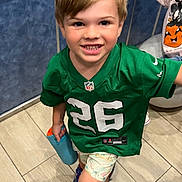 Aaron joined the competition — help win amazing prizes! child, boy, smiling, indoor, green_jersey, sportswear, shorts, shoes, floor, tile_floor, water_bottle, happy, playful, person, face, hair, handrail, background_child, casual_clothing, young