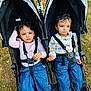 toddler, child, stroller, outdoor, grass, blue_pants, long_sleeve, barefoot, curly_hair, matching_outfits, seatbelt, playground, park, person, two_children, serious_expression, daylight, nature, casual_clothing, sitting