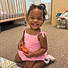 Ahzonni joined the competition — help win amazing prizes! baby_room, cabinet, carpet, child, colorful, crib, curly_hair, dark_skin, girl, happy, indoor, nursery, pink_dress, portrait, reflection, sitting, smiling, toddler, toy, toy_basket