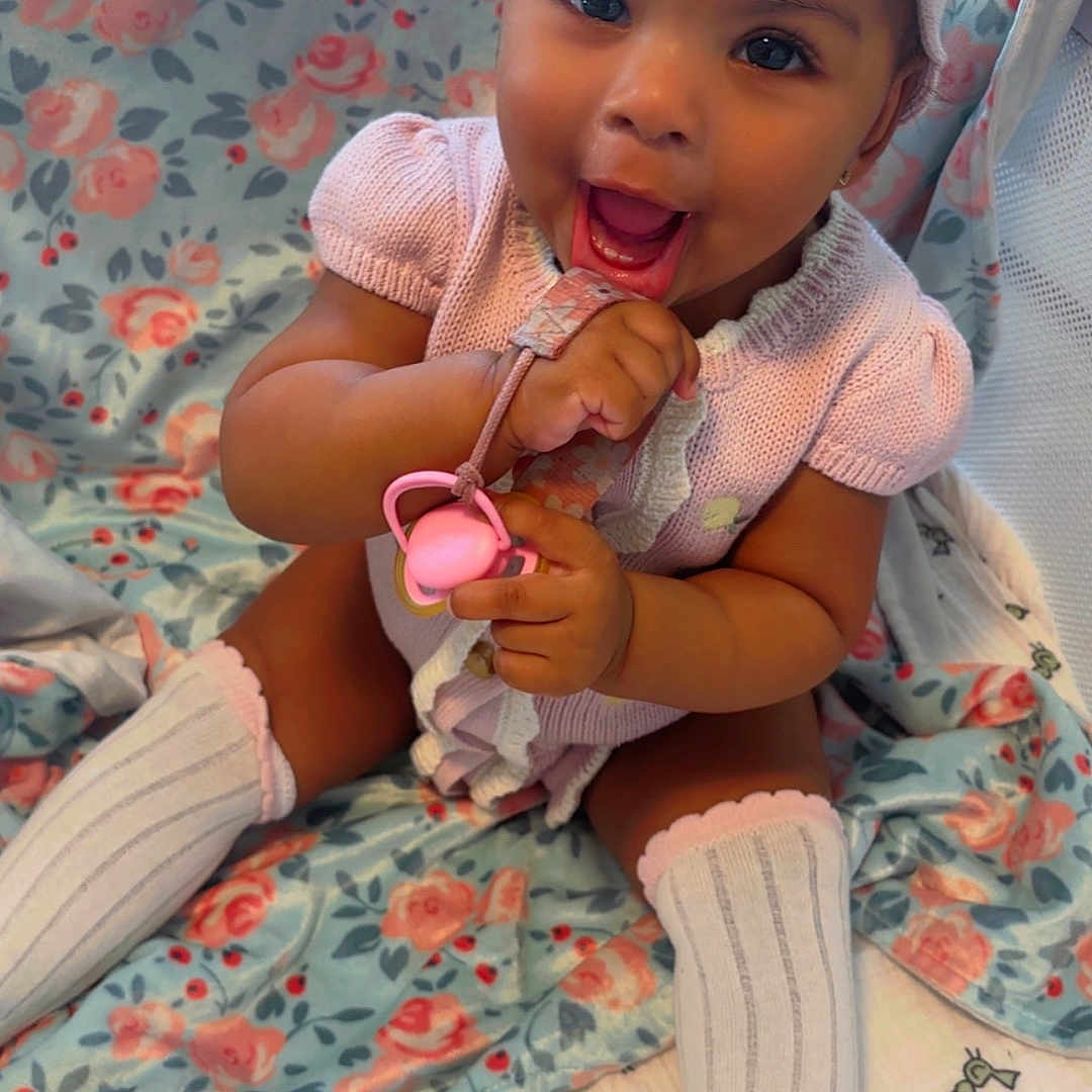 Ahzonni is registered to the contest to win money with this photo: baby, baby_girl, blanket, bow, child, closeup, cute, floral_pattern, happy, headband, indoors, infant, knitted_clothing, pacifier, pink_clothing, playful, portrait, sitting, smiling, white_socks