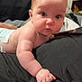 baby, black_fabric, child, chubby_cheeks, close_up, curious, cute, diaper, expression, eyes, face, hand, indoor, infant, lying_down, person, plush, skin, soft, young