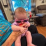 Harper joined the competition — help win amazing prizes! baby, casual, chair, child, couch, curtain, floor, flower, hand, indoor, living_room, person, pink, purple, relaxing, sunglasses, table, toy, window, wood_floor