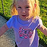 blonde_hair, casual_clothing, child, daylight, front_view, girl, grass, lawn, outdoor, playful, ponytails, portrait, purple_shirt, sidewalk, smiling, standing, summer, sunlight, sunset, toddler