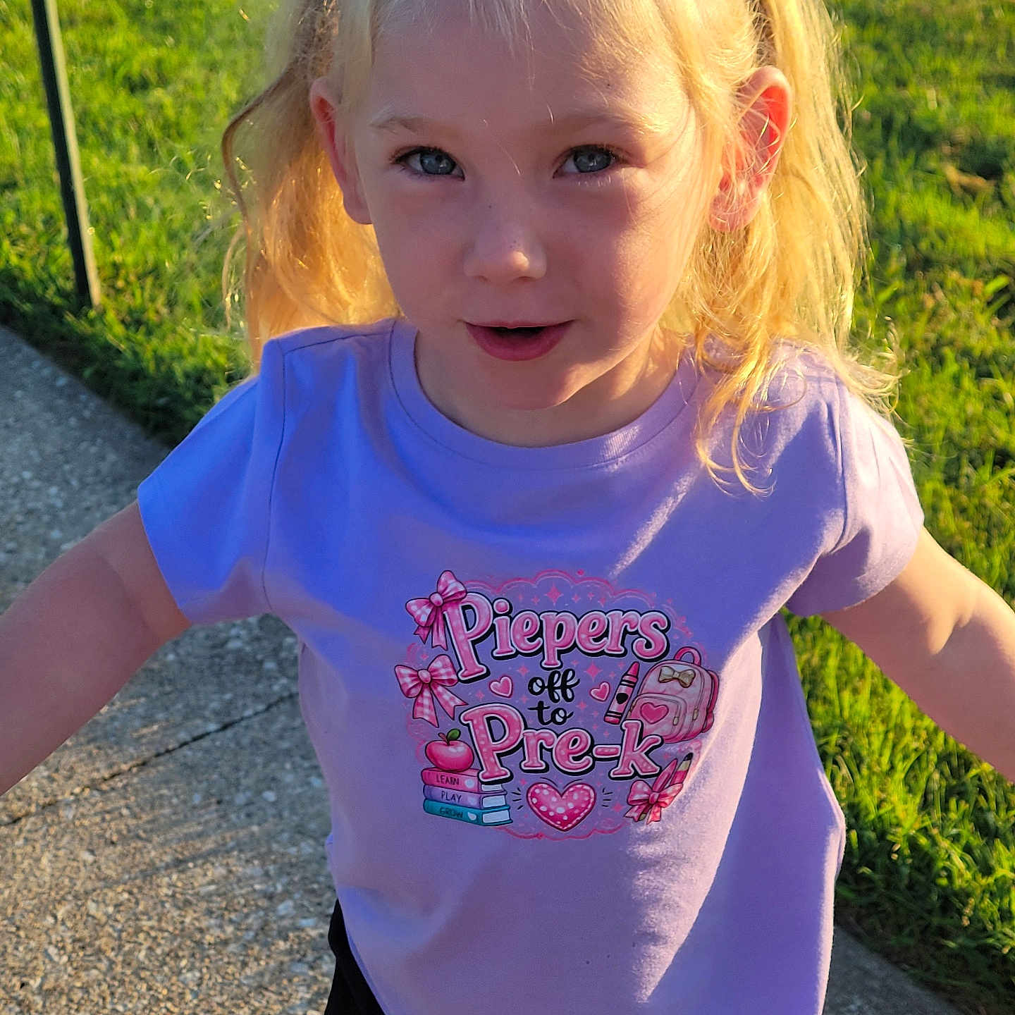 Pieper joined the competition — help win amazing prizes! blonde_hair, casual_clothing, child, daylight, front_view, girl, grass, lawn, outdoor, playful, ponytails, portrait, purple_shirt, sidewalk, smiling, standing, summer, sunlight, sunset, toddler