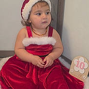 Liyana a rejoint le concours — aidez-le/la à gagner de superbes lots ! 10_months, baby, child, christmas, clothing, cute, expression, face, festive, fur_trim, hands, holiday, indoor, milestone_card, person, portrait, red_dress, santa_hat, sitting, toddler