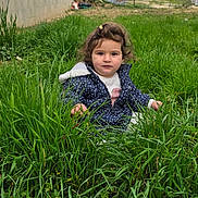 Liyana participe au concours pour gagner de l'argent avec cette photo : blue_jacket, building, child, cute, expression, face, grass, green, ground, hair_clip, hands, jacket, nature, outdoor, polka_dot, portrait, sitting, toddler, wall, yard