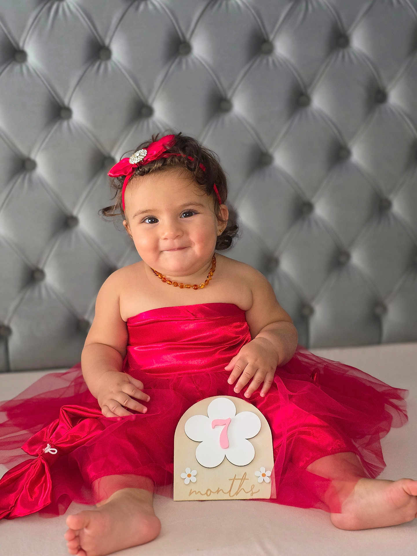 Liyana participe au concours pour gagner de l'argent avec cette photo : baby, barefoot, bed, child, cute, happy, headband, indoor, infant, jewelry, milestone, months, person, portrait, red_dress, sign, sitting, smile, tufted_headboard, tulle