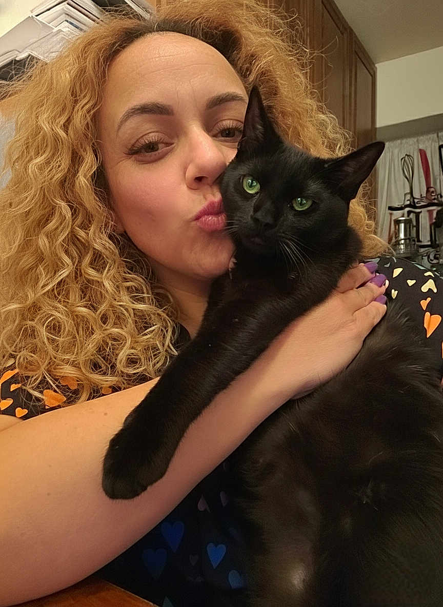 Dex Starr is registered to the contest to win money with this photo: woman, cat, black_cat, curly_hair, green_eyes, indoor, kitchen, affection, holding, portrait, close_up, love, pet, animal, human, face, smile, furniture, curtains, nails