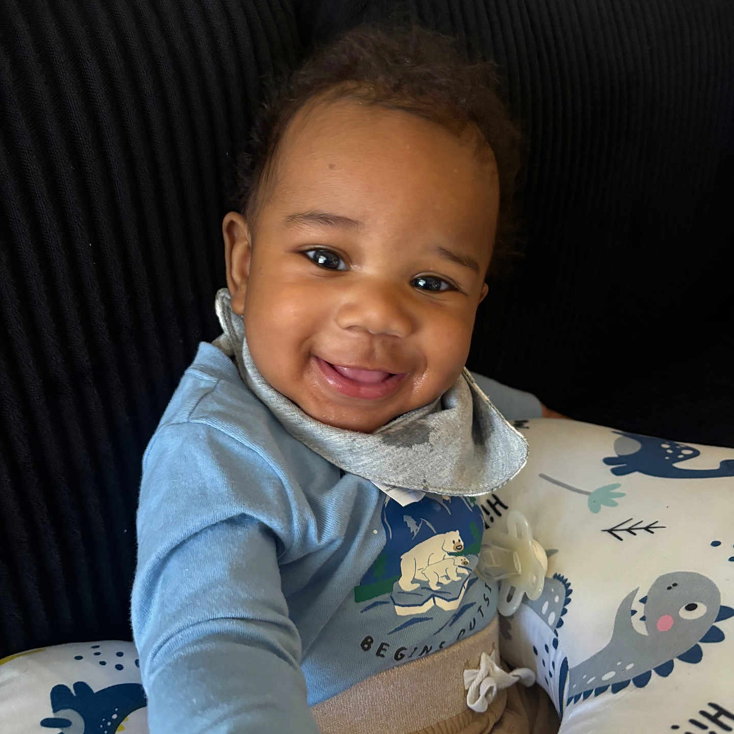 Ronald joined the competition — help win amazing prizes! baby, blue_shirt, child, clothing, comfort, cozy, cushion, cute, dinosaur_pattern, face, hand, happy, home, indoor, infant, pacifier, portrait, seated, smiling, toddler